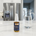 Quicksilver Scientific Liposomal Vitamin C pump bottle on white quartz kitchen island next to refrigerator and open glass water pitcher