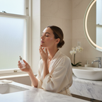 Lifestyle image - woman with glowing skin applying serum in bright bathroom, luxury skincare lifestyle editorial for visual context only