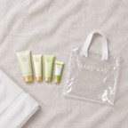 Flat lay of Mary Kay Satin Hands travel tubes beside clear Mary Kay tote and towel