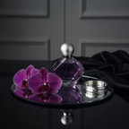 Lifestyle — purple perfume spray bottle on mirrored vanity tray beside dark purple orchids, silver bangle bracelet, and folded black silk — moody elegant editorial for visual context only