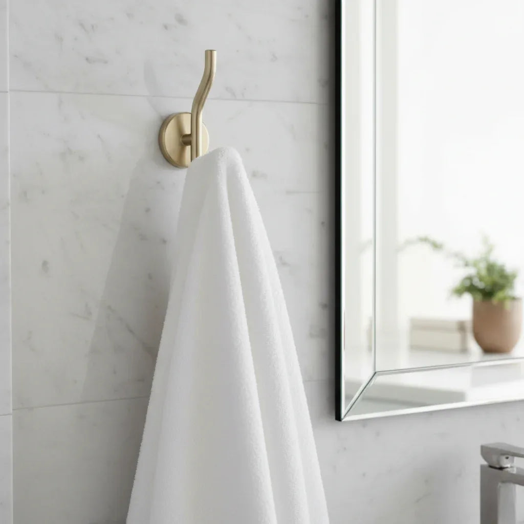 Luxury modern bathroom with Delta Trinsic champagne bronze robe hook holding a white fluffy towel on marble wall