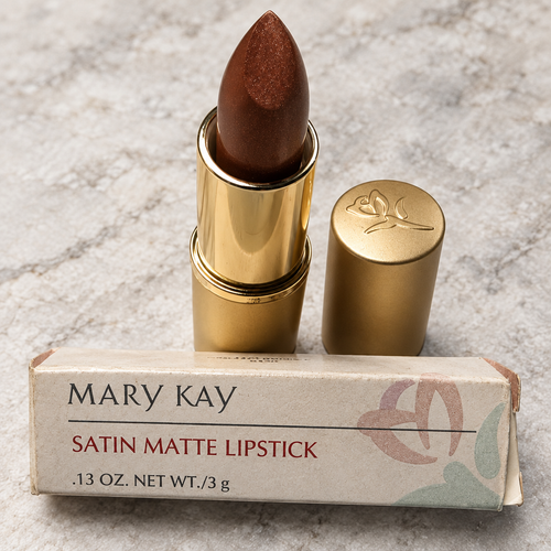 Close view of Mary Kay Bistro Bronze 4199 lipstick, gold cap and retail box on stone