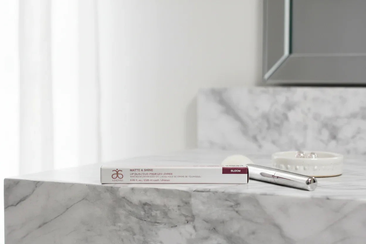 Arbonne Matte and Shine Lip Duo Bloom on marble makeup vanity with natural daylight lifestyle