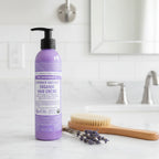 Dr. Bronner's Lavender Coconut Organic Hair Creme purple pump bottle on bathroom vanity next to wooden paddle brush and dried lavender sprig