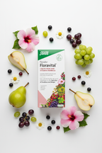Salus Floradix Floravital Liquid Iron and Vitamin Formula 500ml box flat lay with fresh grapes, pears, black currants, hibiscus blooms, and chamomile flowers on a white surface – More4less Outlet