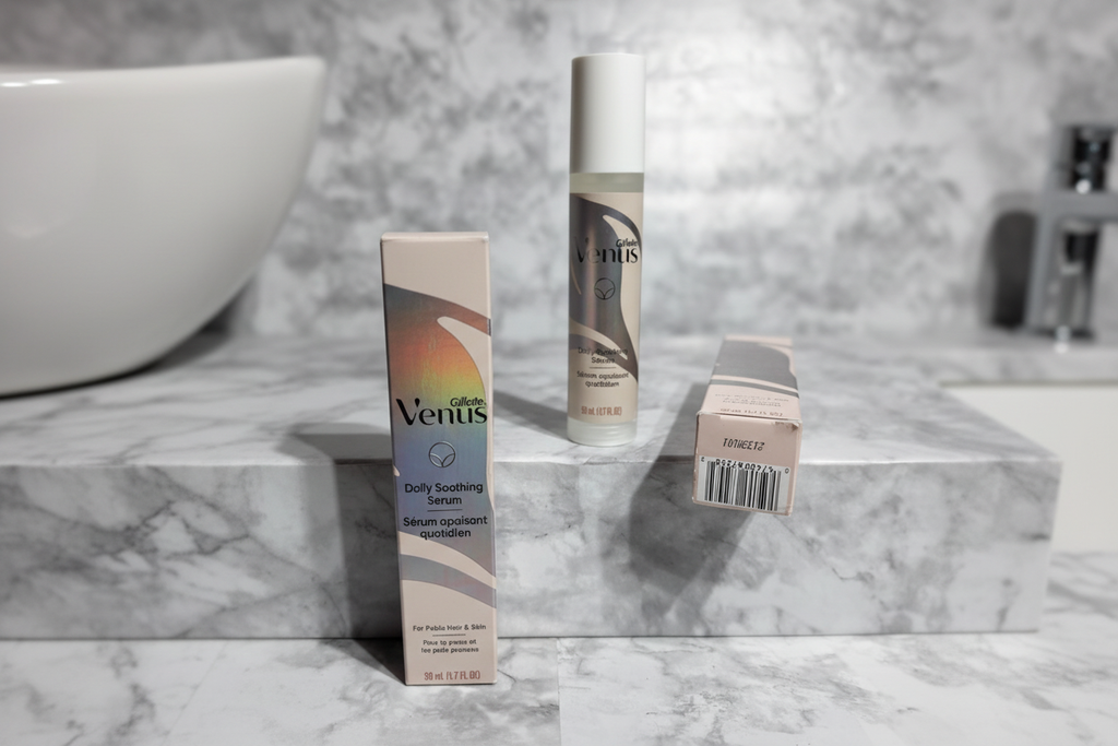 Gillette Venus Daily Soothing Serum slim pump bottle with white cap and holographic label alongside retail carton on white marble vanity in soft natural light
