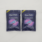 Two sealed DenTek Sensitive Gums Comfort Clean floss pick bags on a light surface