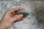Close-up of a human hand calmly holding and rotating a smooth oval sensory fidget stone with tactile ball bearings