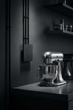 Legrand Adorne graphite screwless wall plate installed on dark charcoal wall in modern industrial kitchen next to chrome countertop mixer