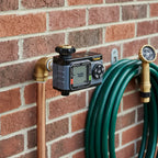 Melnor XT HydroLogic Digital Water Timer installed on copper outdoor spigot on brick exterior wall next to coiled green garden hose
