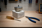 Screwdriver and needle-nose pliers next to a replacement stove infinite switch on a workbench