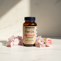 Lifestyle context image of Wiley's Finest Prenatal DHA Fish Oil 180 softgels (AI-generated for visual illustration only) – white marble surface with pink flowers – More4less Outlet