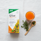 Salus Floradix Epresat Liquid Multivitamin on white linen with supplement glass, fresh herbs, and wooden spoon.
