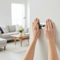 Person using thumbs to press steel wall hanger into drywall in modern living room