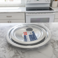 GE Appliances GE68C Chrome Drip Bowl Set 4-Pack in original factory shrink wrap on a white marble kitchen countertop beside a modern electric range