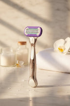 Soft morning light illuminating a premium platinum-finish women's razor in a spa-like bathroom setting on white marble