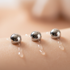 Macro close-up of three shiny metal rollerballs gliding over smooth skin with clear hydrating sheen