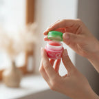 Close-up hands opening a colorful Noro cosmetic lip balm jar with shallow depth of field