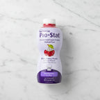 Overhead flat lay of Nutricia Pro-Stat liquid protein supplement bottle on white marble surface, bright even studio lighting