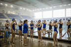 Swim coach handing goggles to competitive swimmers on pool deck, indoor aquatic center
