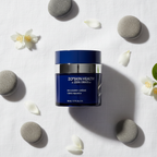 ZO Skin Health Recovery Crème navy blue jar flat lay on white linen with river stones and jasmine petals