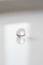 Close-up of a drop of clear facial serum reflecting clean natural daylight on smooth white surface