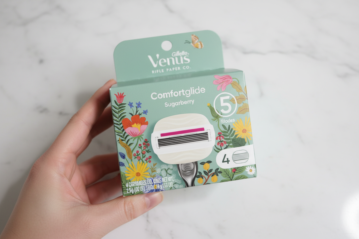 Hand holding Gillette Venus Comfortglide Sugarberry Rifle Paper Co. limited edition box with botanical floral design against white marble tile