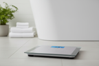 Taylor Digital Bath Scale on grey bathroom tile floor beside white bathtub with towels and plant