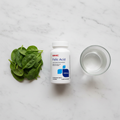 GNC Folic Acid bottle on marble with fresh spinach leaves and glass of water – More4less Outlet