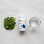 GNC Folic Acid bottle on marble with fresh spinach leaves and glass of water – More4less Outlet