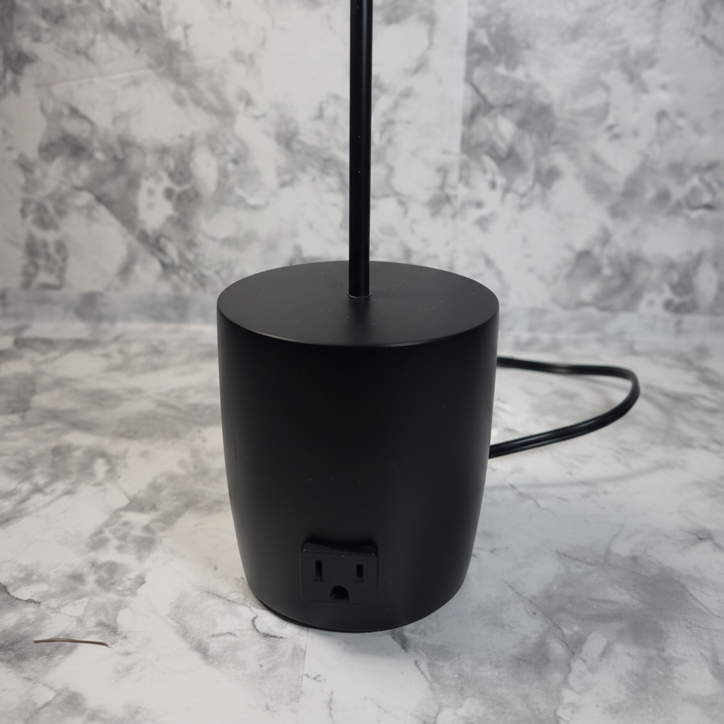 Close detail of the black desk lamp base and single AC outlet