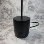 Close detail of the black desk lamp base and single AC outlet