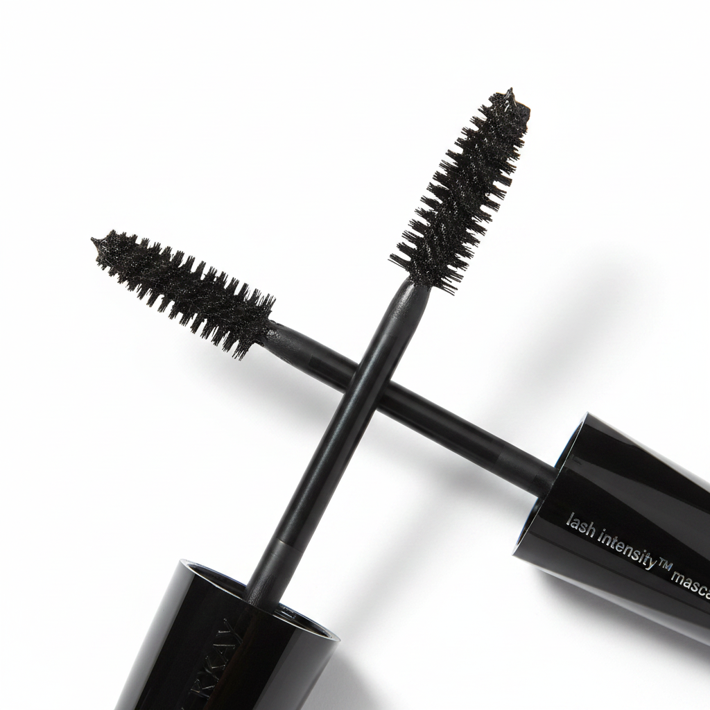 Close-up macro of Mary Kay Lash Intensity Mascara wand pulled from its angular black tube — showing the asymmetrical Double-Impact brush with short and long bristles loaded with rich black mascara formula on a white background