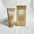 Bright airy studio composition of Jergens Natural Glow gold squeeze tube face moisturizer and box on white linen surface