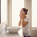 Woman lathering gel cleanser on her face in circular motions at a bathroom sink during morning skincare routine
