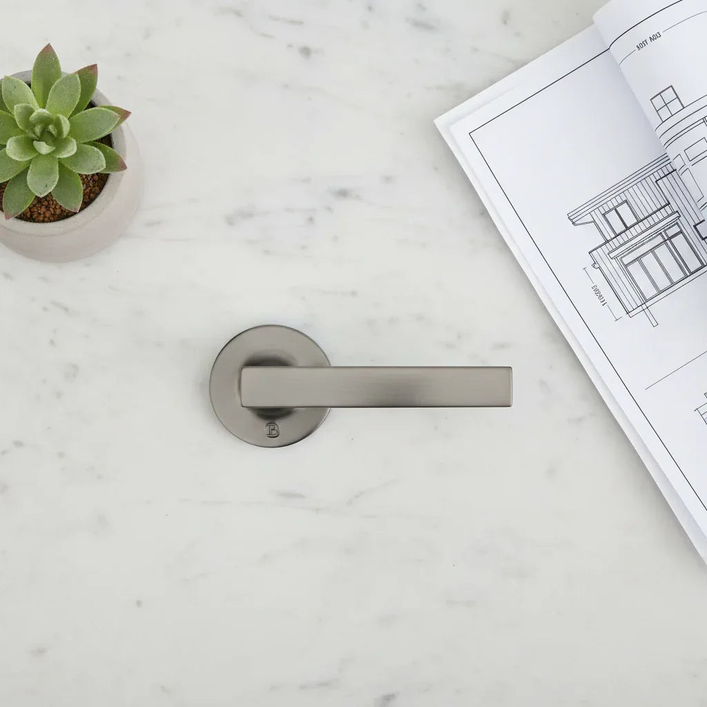 Baldwin Reserve contemporary half-dummy door lever flatlay on white marble surface with architectural blueprints