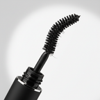 Macro close-up of flexible silicone mascara wand pulled from sleek black tube showing fine bristles coated in deep black formula