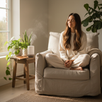 Woman sitting in cozy reading chair in calm mindfulness with small diffuser misting on side table and green plants nearby