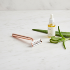 Sleek modern razor on white marble countertop beside botanical oil and aloe vera
