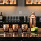 Four hammered copper-finish mini Moscow Mule shot mugs on polished black marble bar with cocktail shaker and sliced lime