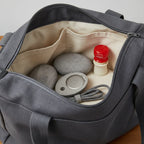 Lifelines grounding stones and oil bottle in open tote bag showing wellness on the go portability.