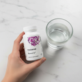 Hand holding Thorne ResveraCel white bottle with purple watercolor design beside glass of water on marble countertop morning wellness