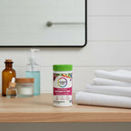 Rainbow Light Women's One Multivitamin bottle on light-wood bathroom vanity shelf with white linen towels and glass apothecary items