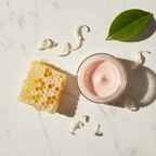 Flat lay of moisturizing cream with beeswax honeycomb and wax shavings on white marble surface