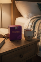 Purple Yogi Wellness Blends tea gift box on a cozy nightstand next to a book and a steaming mug of bedtime tea with warm ambient bedroom lighting.