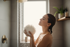 Woman in modern bathroom holding loofah with rich soap suds during relaxing morning shower
