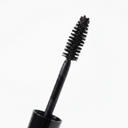 Close-up macro of Mary Kay Lash Love Lengthening Mascara wand pulled from its glossy black tube — showing the flexible sculpted brush with fine bristles coated in rich black mascara formula on a white background