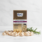 RoC Retinol Correxion Night Serum Capsules box on marble with scattered pearl capsules and rosemary.