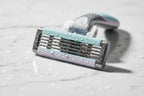 Close-up of water droplets on a high-quality 5-blade women's razor cartridge on white marble