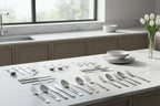 Clean minimal kitchen interior display of polished stainless steel flatware on white marble surface